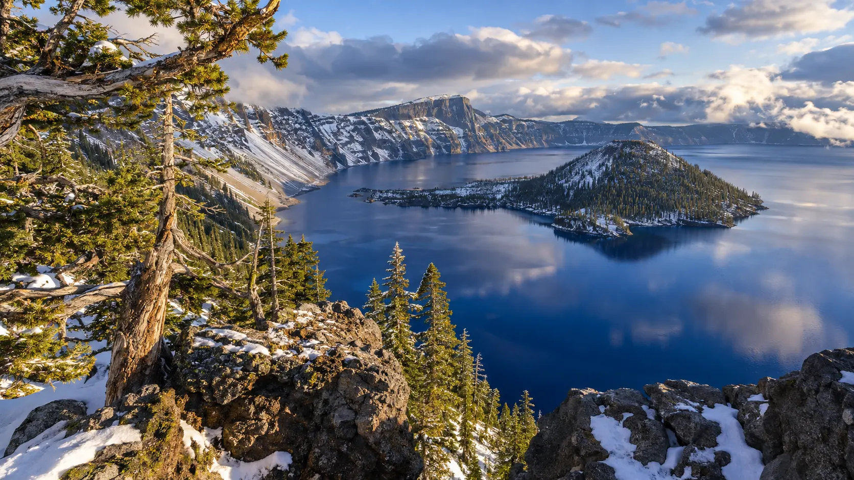 Wizard Island surrounded by the deep blue water and snowy rim of Crater Lake, Oregon.