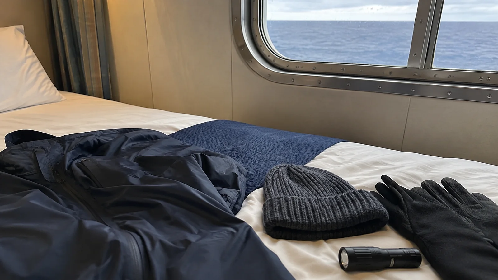 Warm jacket, knit hat, gloves and flashlight laid out on a cabin bed.