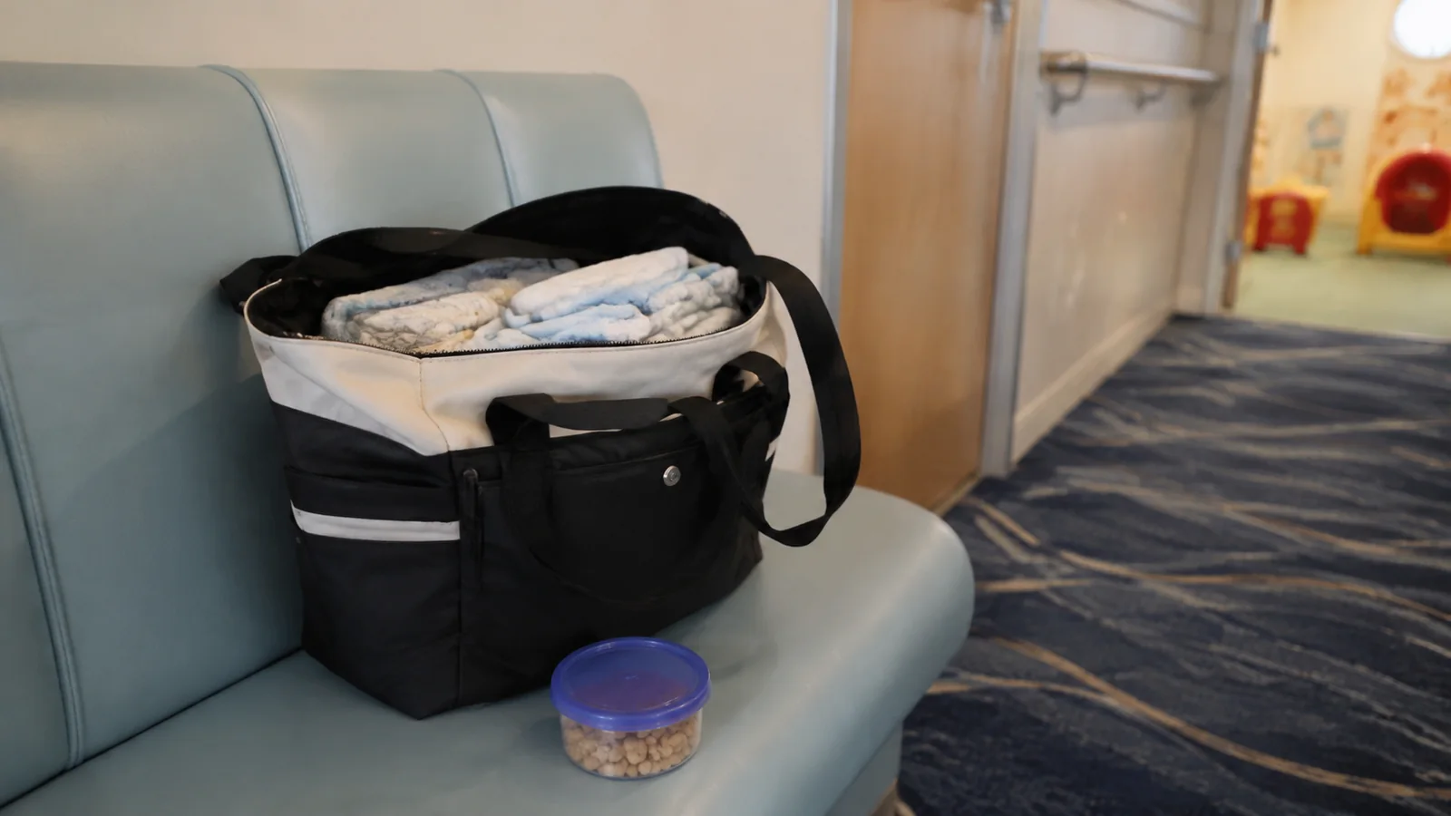 Open diaper bag with folded supplies and a small container on a chair.