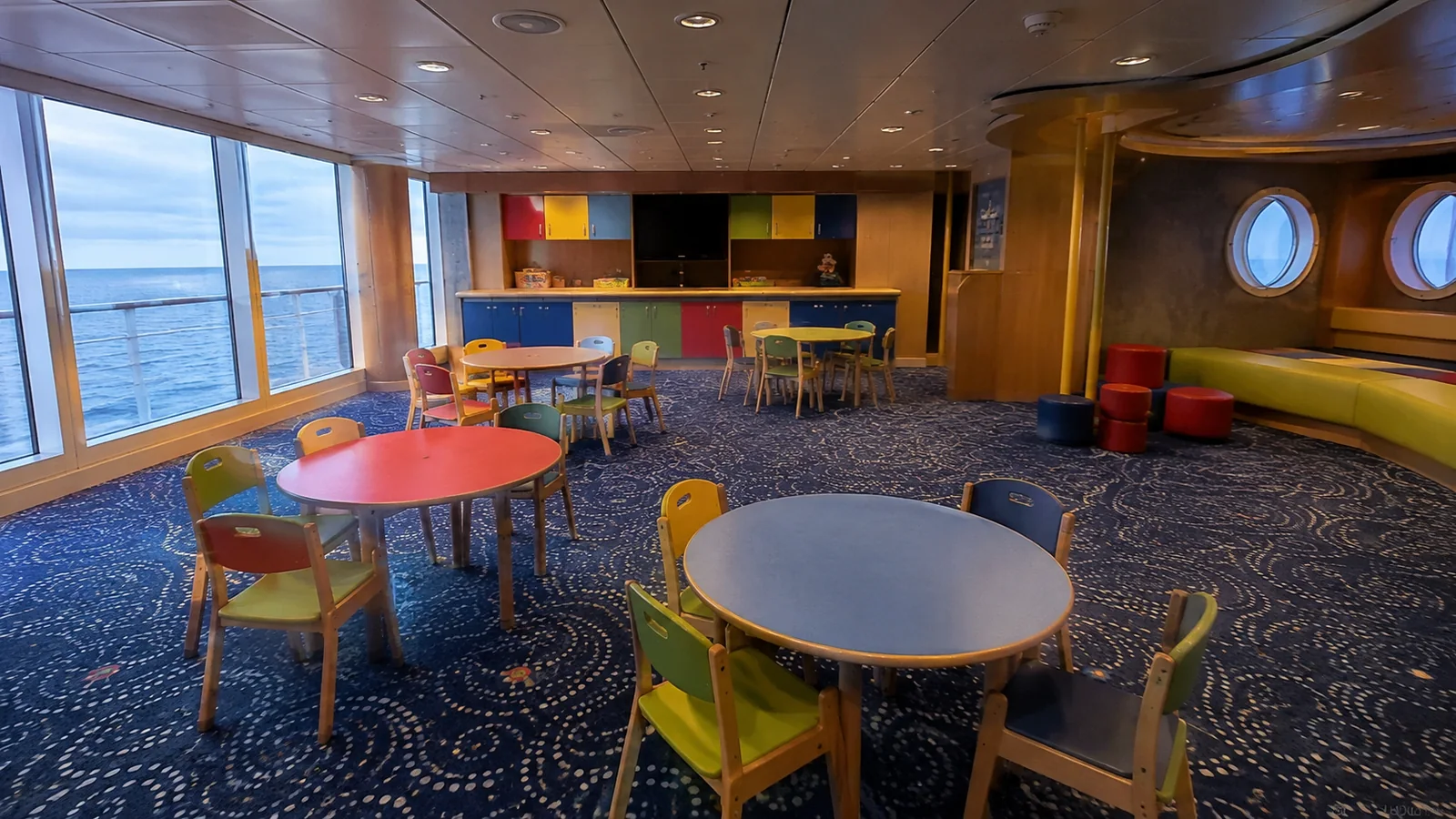 Empty children's activity room with colorful tables and ocean windows.