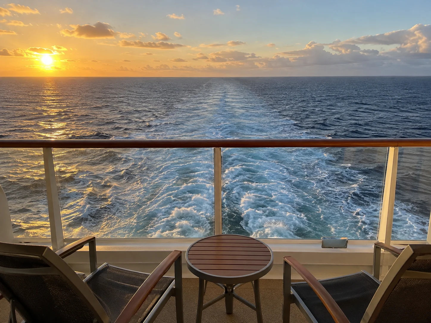 Aft-facing cruise balcony overlooking the ship's wake at sunset.