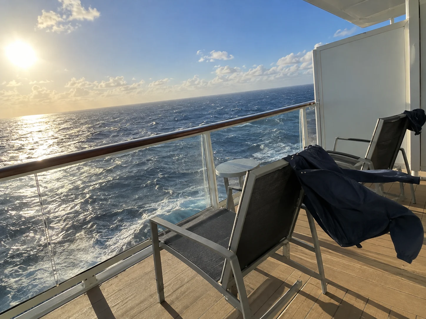 Windy high-deck cruise balcony with chairs and a jacket blowing in the breeze.