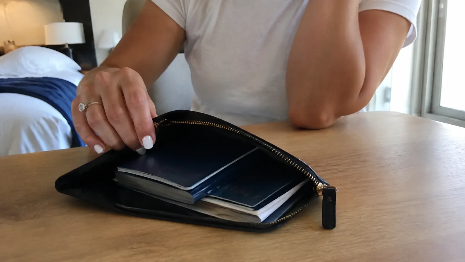 Hand opens a zipped wallet containing several dark travel booklets.