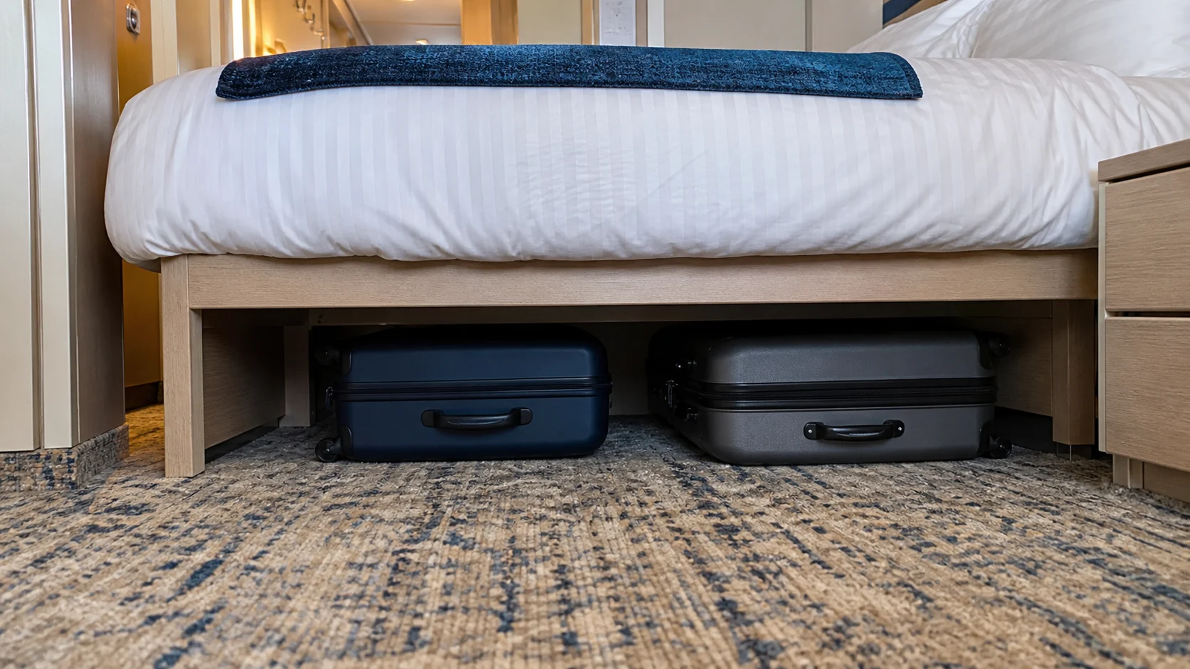 Open storage space beneath a cruise cabin bed with unpacked suitcases tucked out of sight