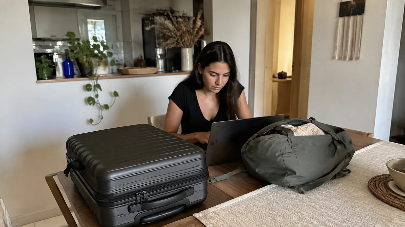 Woman uses a laptop at a table surrounded by travel bags.