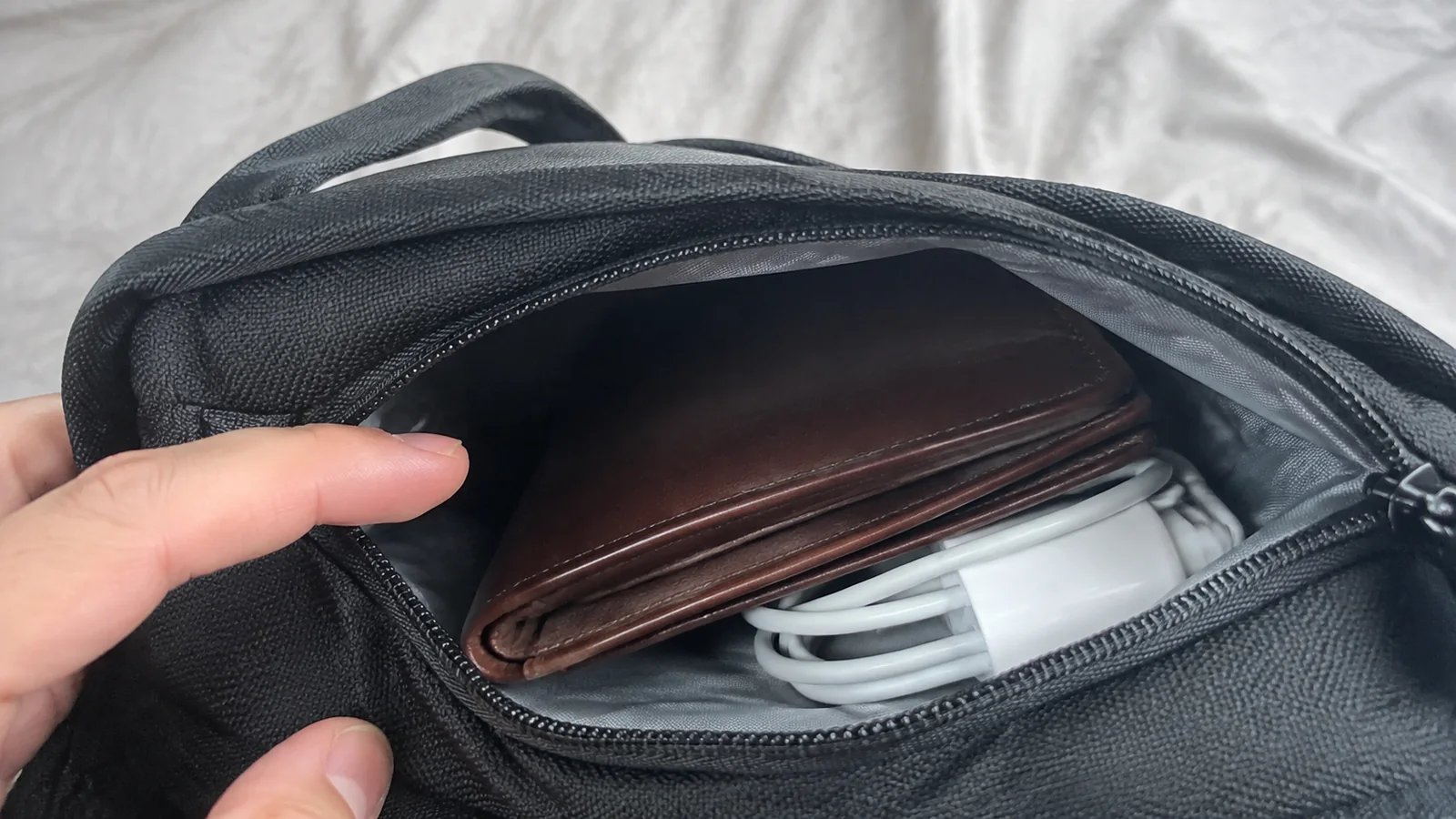 Open bag pocket contains a brown wallet and white charger.