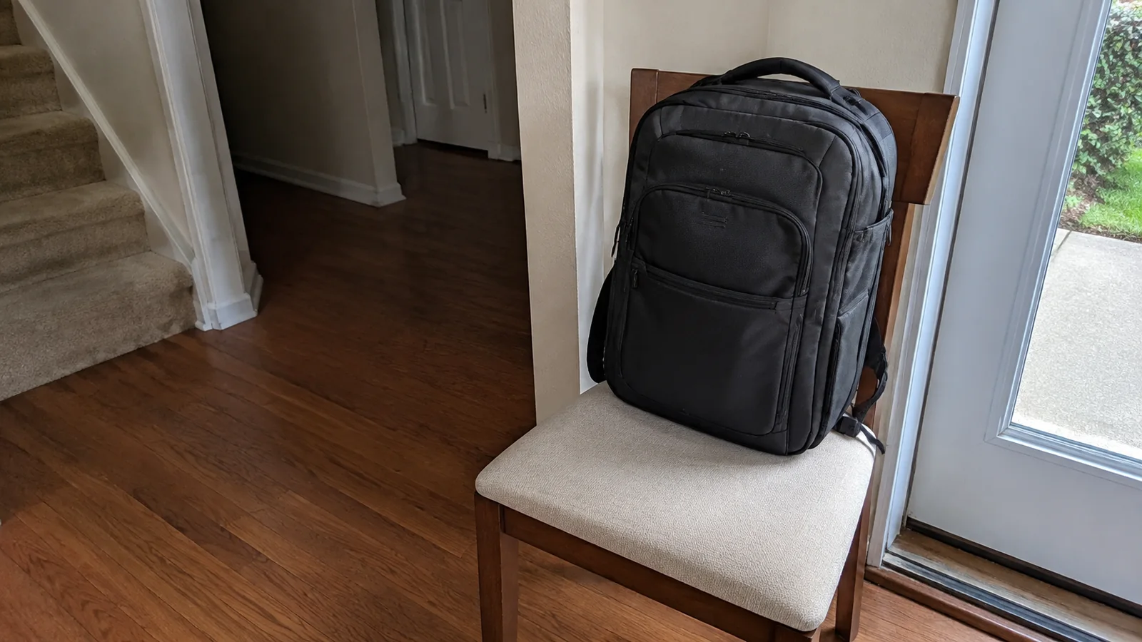 Black backpack stands on a chair beside an open doorway.