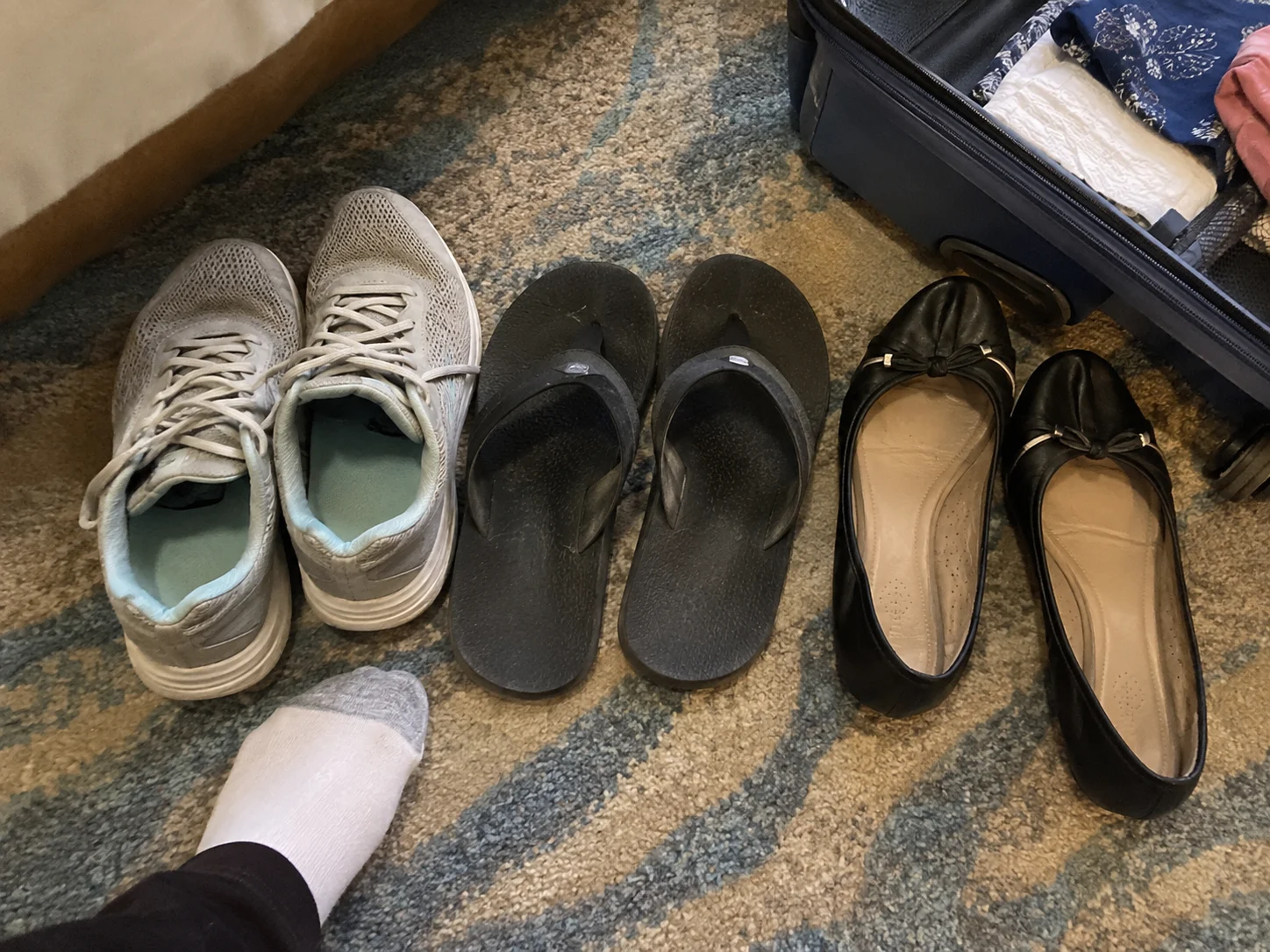 Walking sneakers, pool sandals and dress flats sit beside an open suitcase.