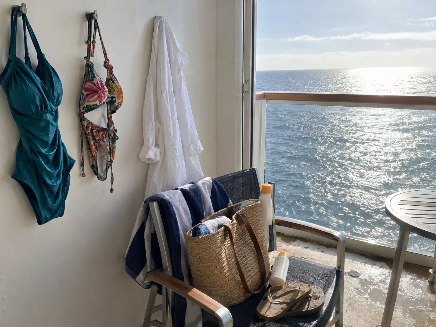 Swimwear and a linen cover-up dry beside a cruise cabin balcony door.