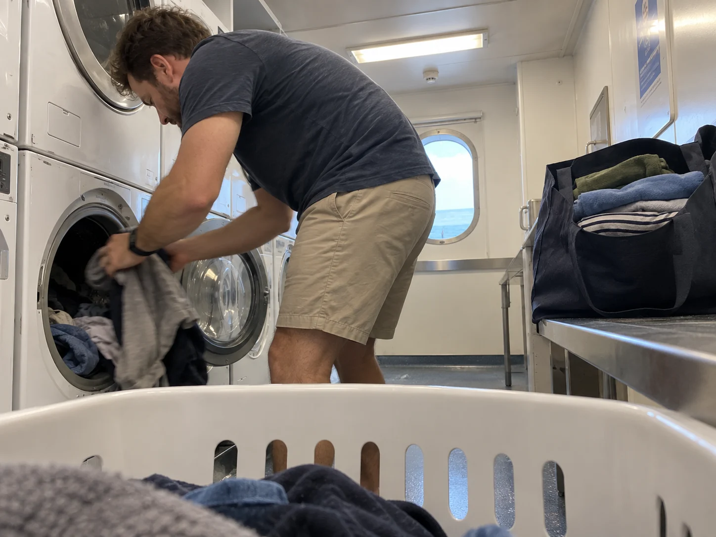 A traveler transfers casual clothes in a cruise self-service laundry room.