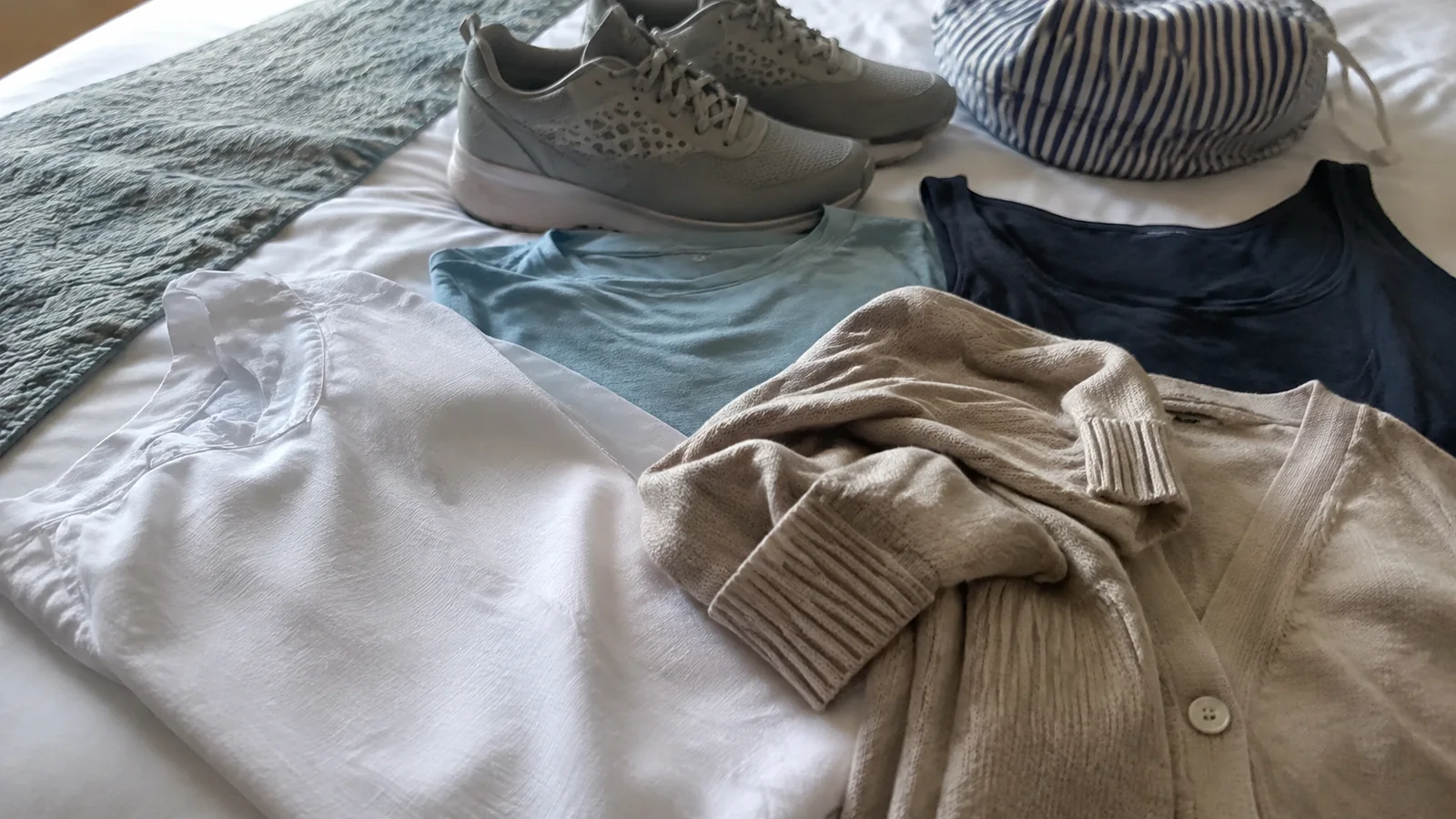 Walking shoes, a hat and layered clothing arranged on a bed.