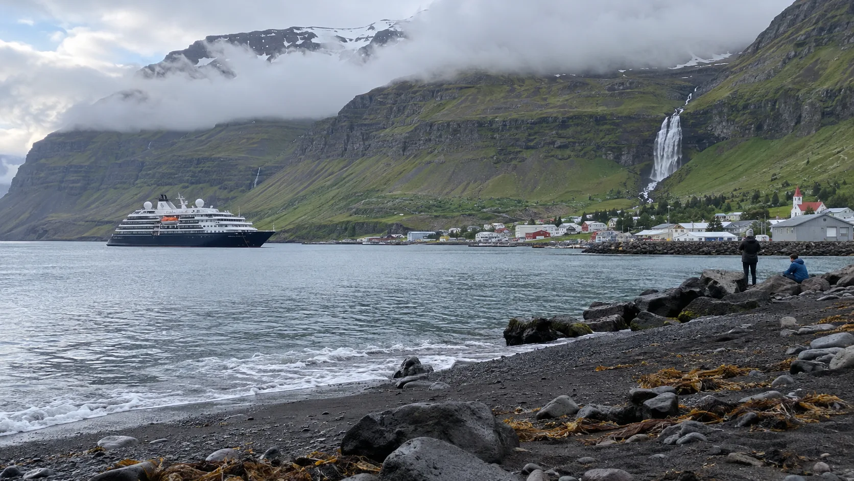 Cruise ship anchored by an Icelandic fjord village and waterfall