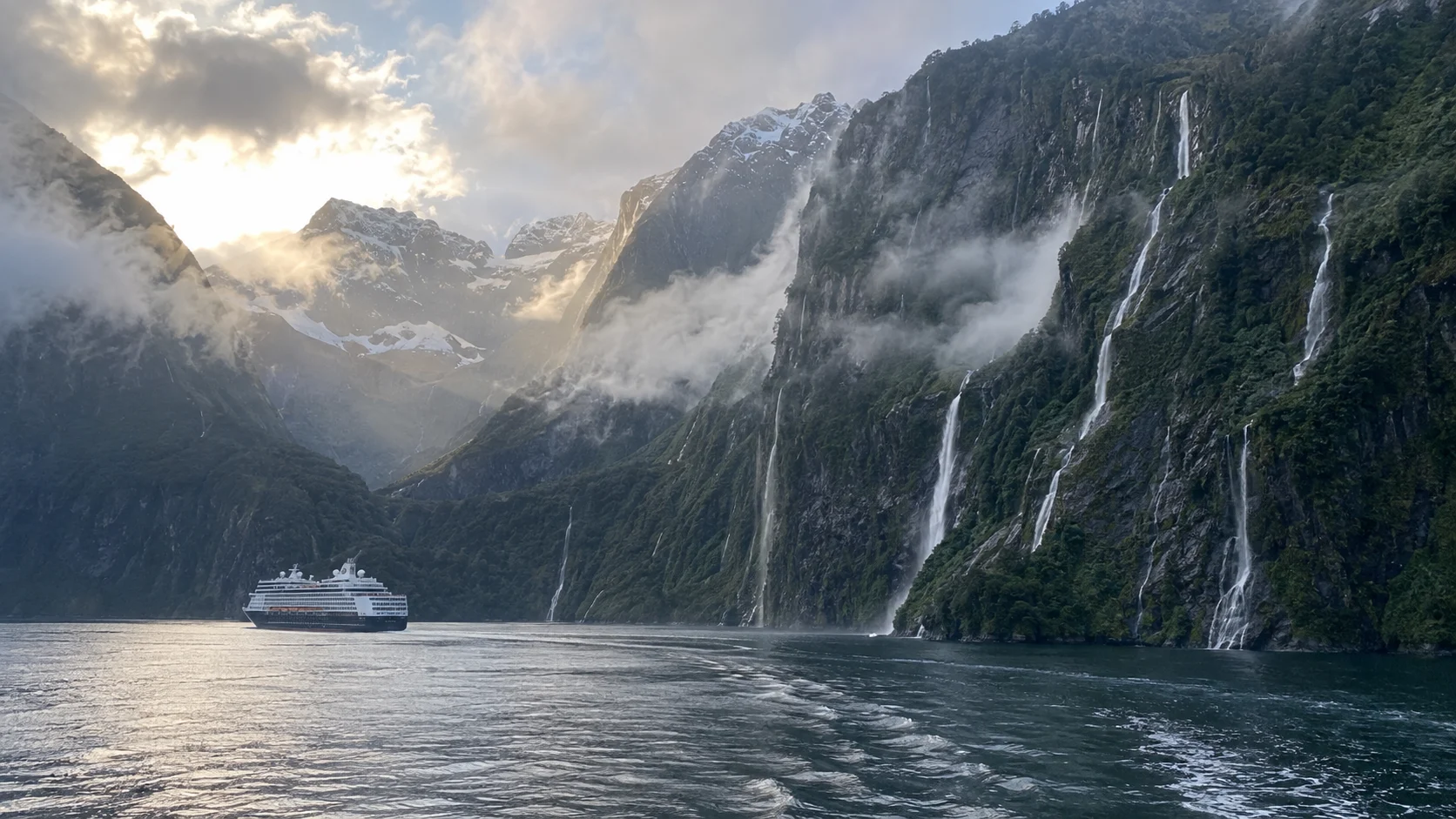 Cruise ship sailing through Milford Sound beneath mountains and waterfalls