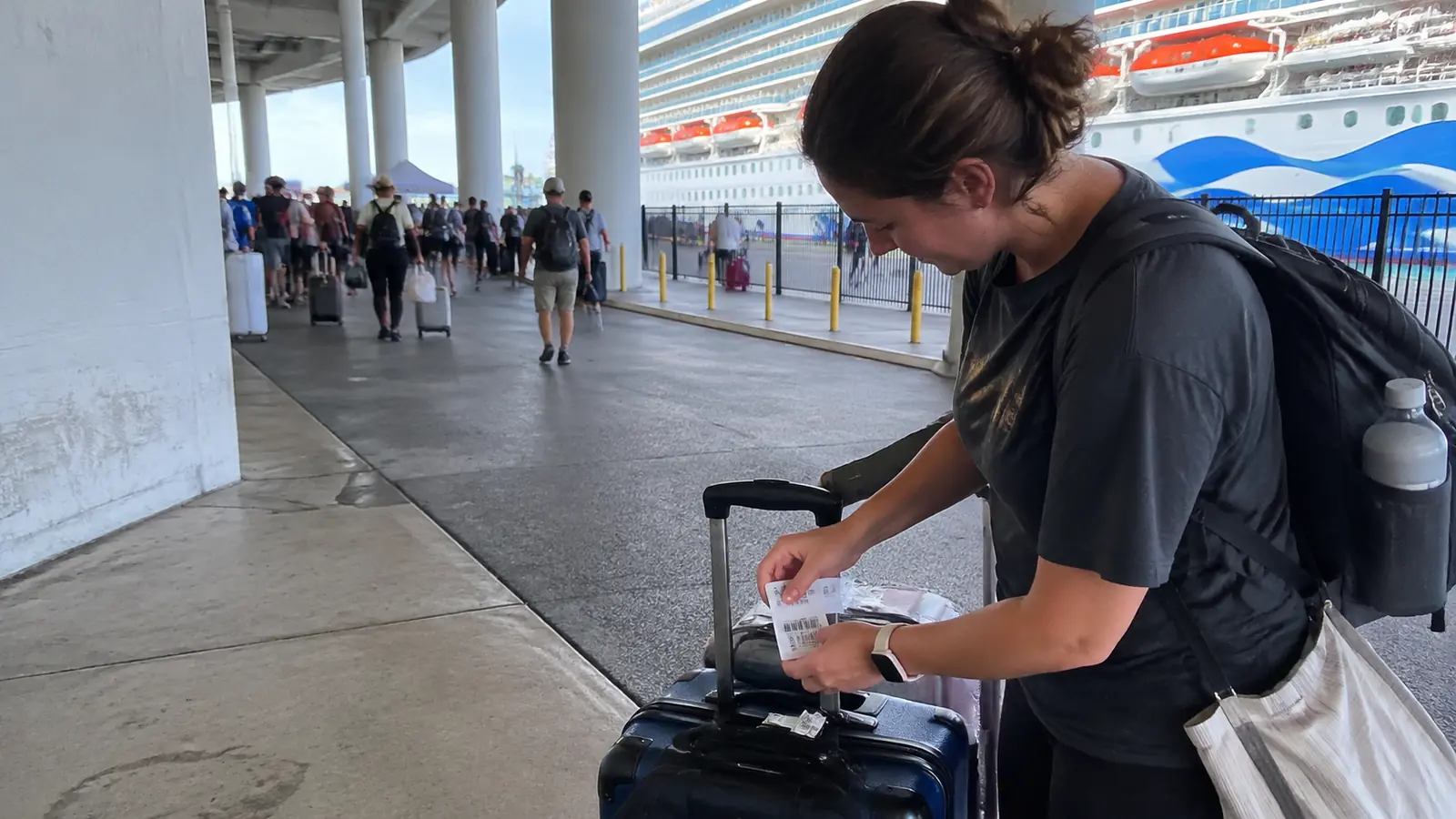 Woman attaching a luggage tag to a suitcase near a cruise terminal