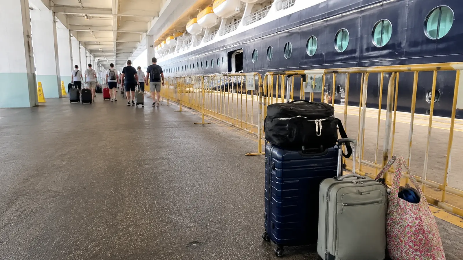 Several suitcases lined up on a pier beside a docked cruise ship