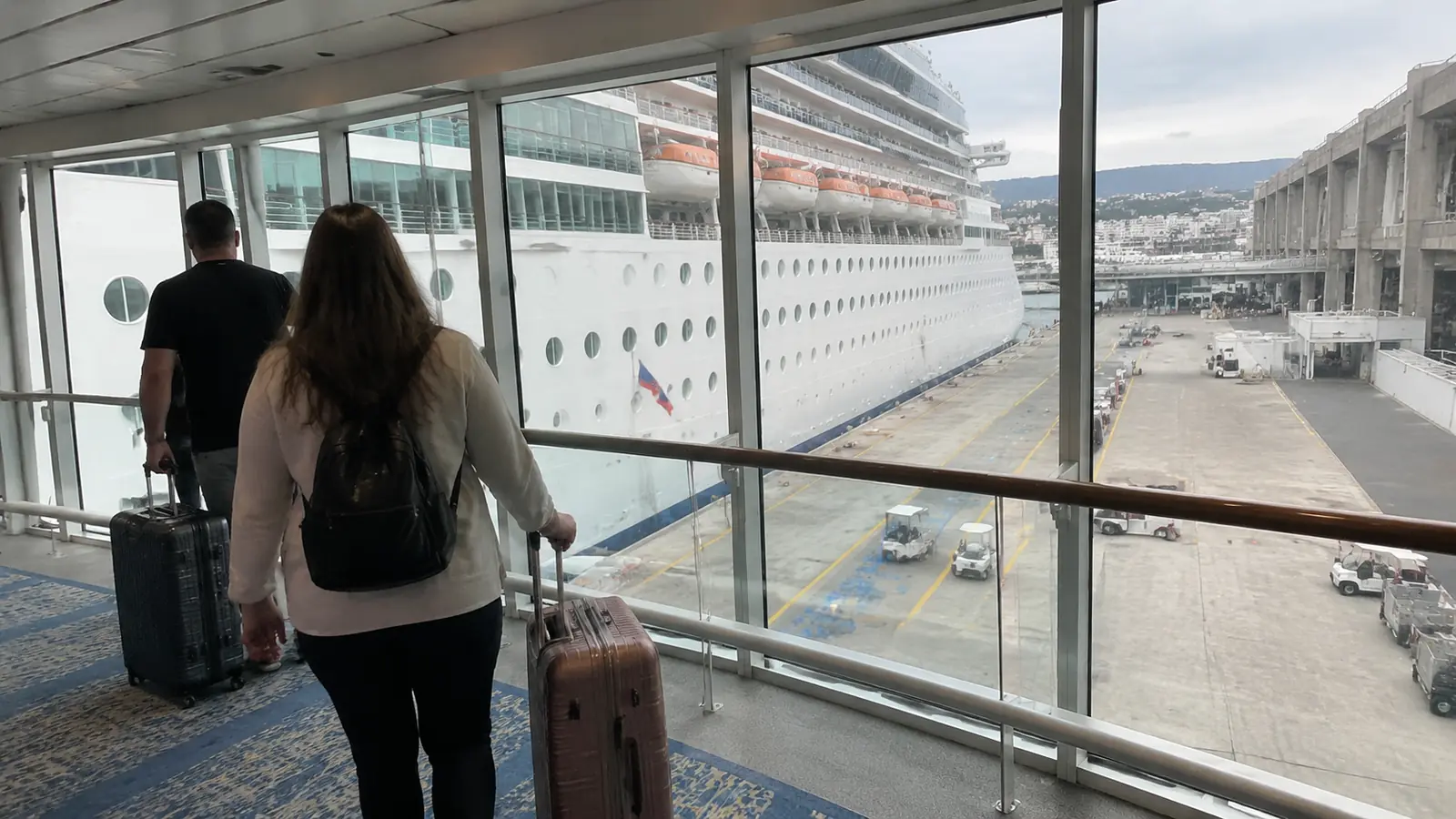 Travelers pulling suitcases through a covered cruise terminal walkway