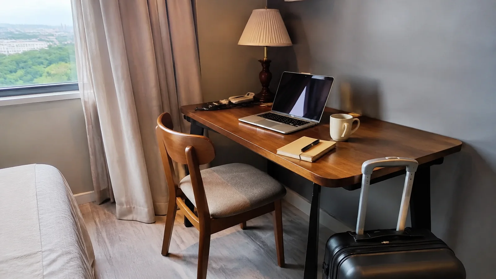Small table beside a window holds a laptop, books and mug.