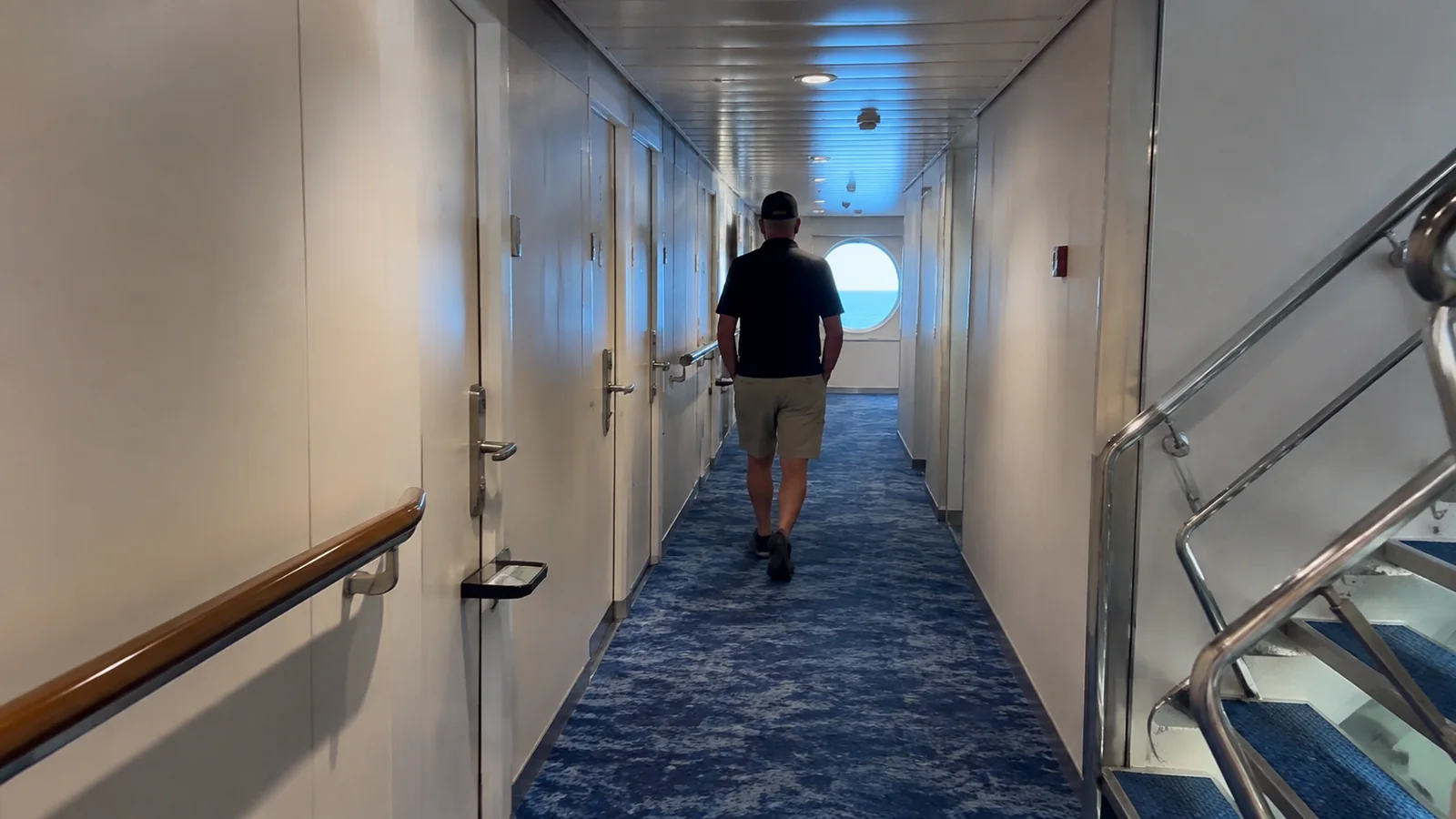 Passenger walking past a stairwell in a cabin corridor.