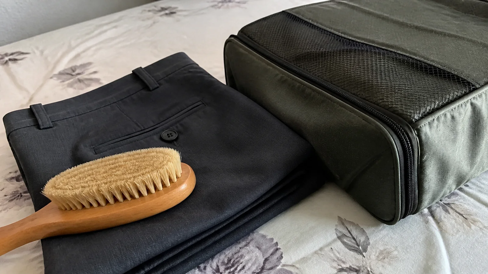 Clothes brush resting on dark trousers beside a toiletry bag.