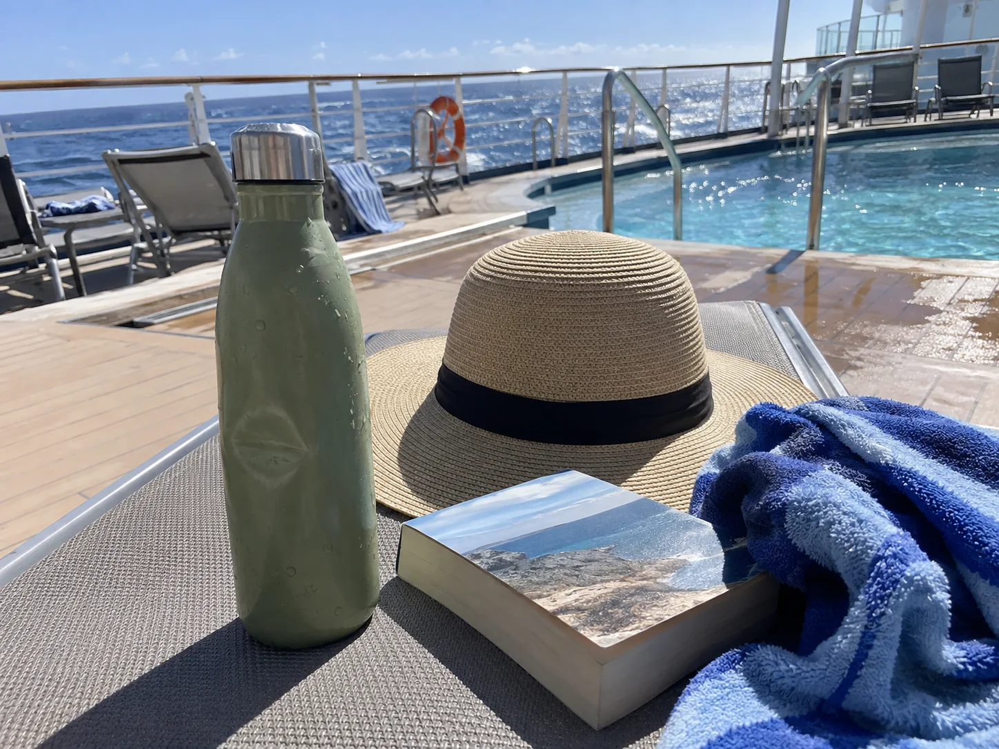 Insulated water bottle beside a sunhat on a cruise ship deck chair