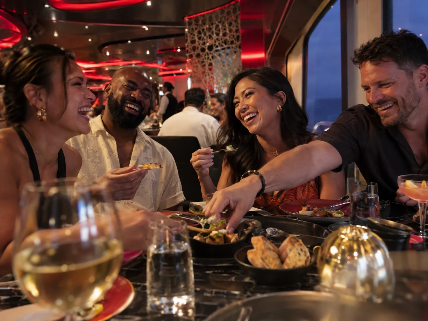 Adult friends laughing over small plates in a contemporary cruise restaurant.