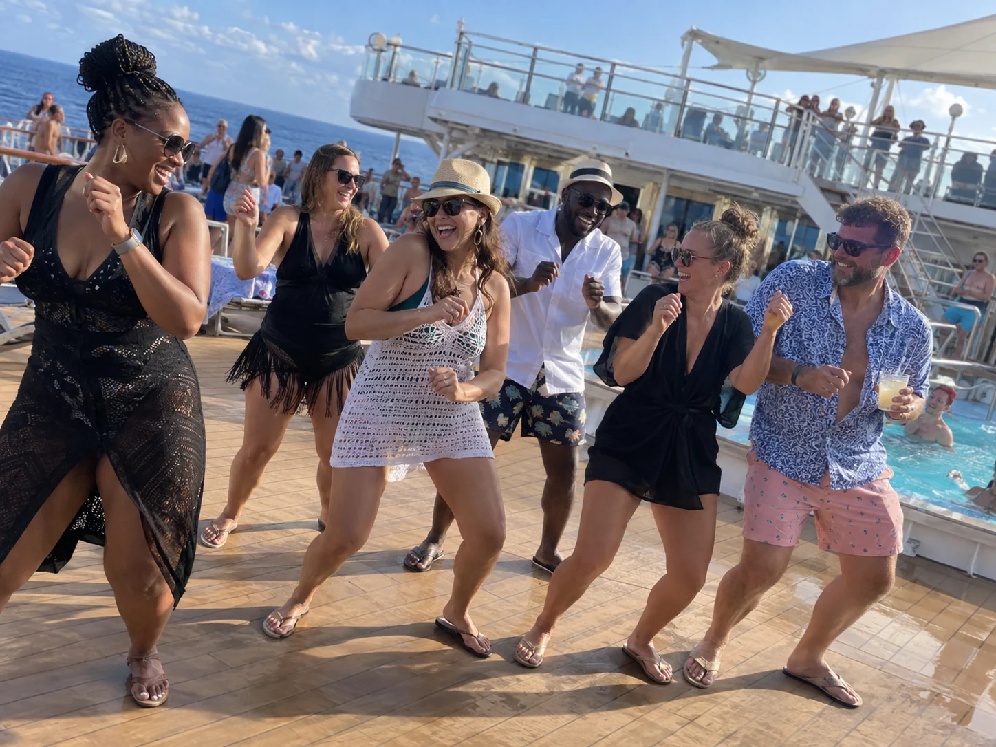 Friends dancing together beside a sunny cruise ship pool deck.