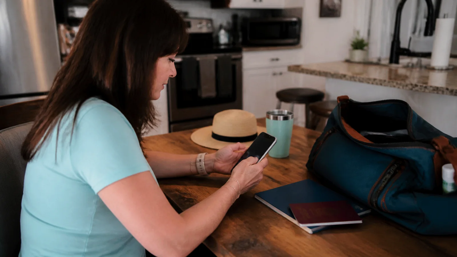 Woman checks her phone beside travel bags on a table.