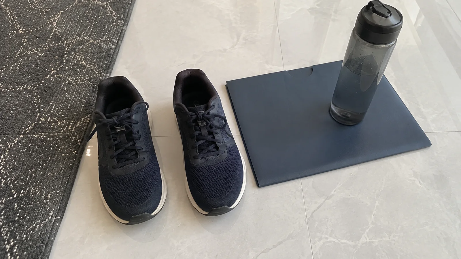 Dark sneakers, folder and water bottle are arranged on the floor.
