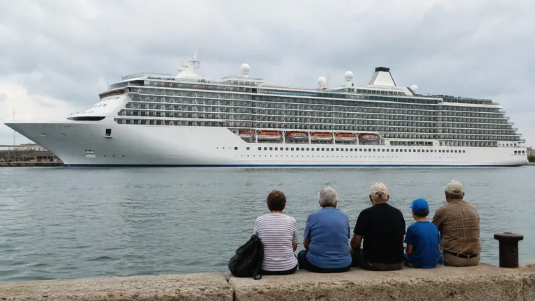 Family seated on a quay watching a large cruise ship across the water.