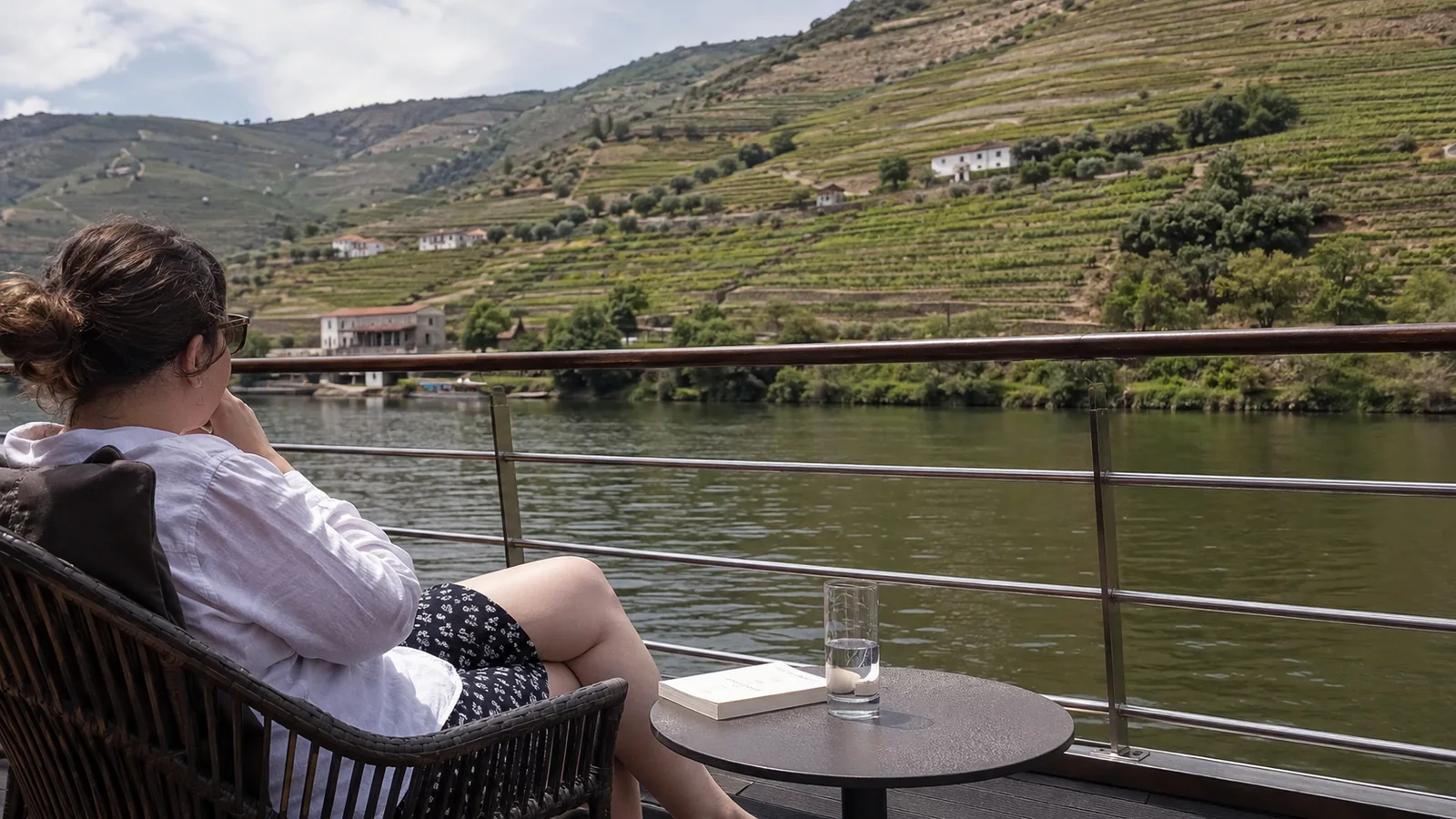Passenger relaxing on a river-cruise deck beside terraced green hills.