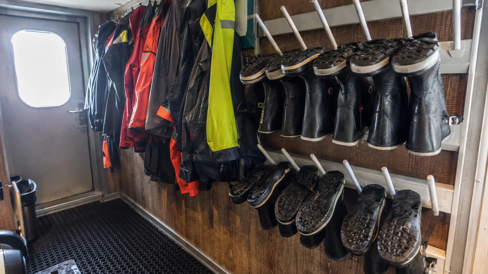 Waterproof jackets and rubber boots stored in an expedition-ship gear room.