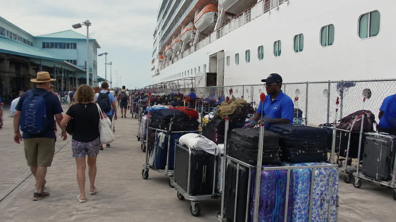 Porters stand beside luggage carts as travelers approach a ship.