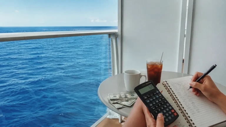 Woman using a calculator and writing in a notebook at a cruise ship balcony table