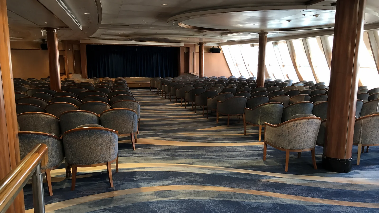 Rows of empty chairs face a stage inside a ship lounge.