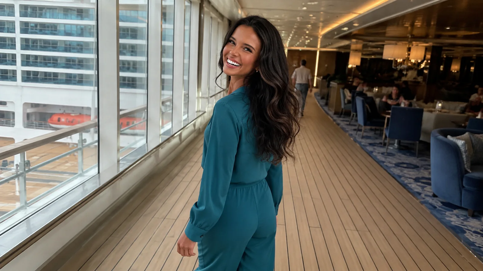 Woman stands in a bright ship corridor beside large windows.