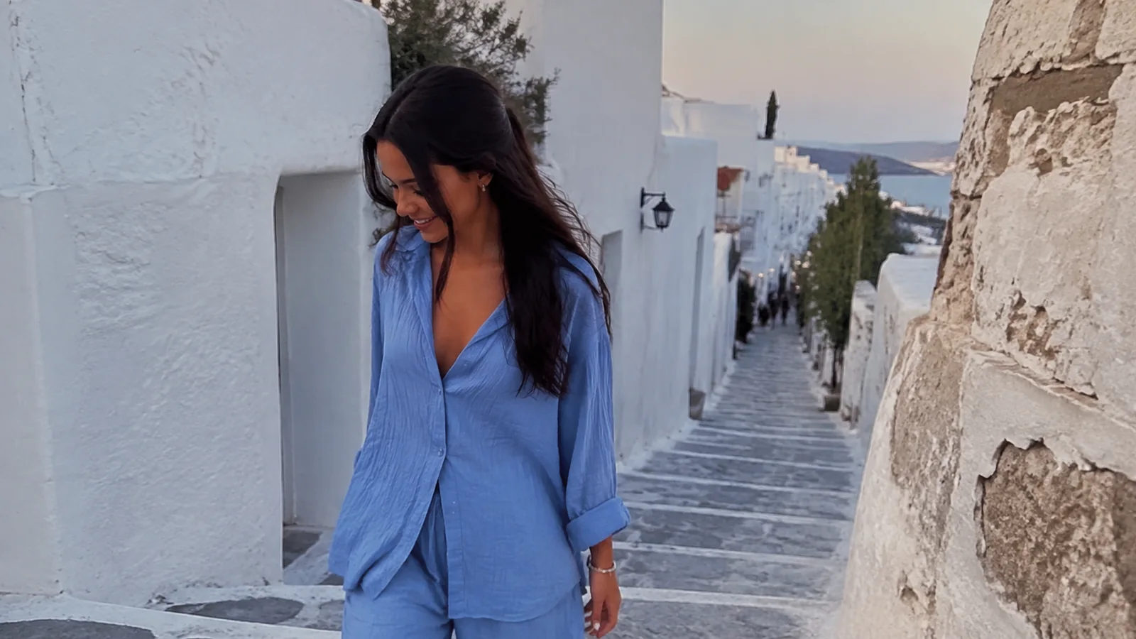Woman walking down stone steps between whitewashed buildings.