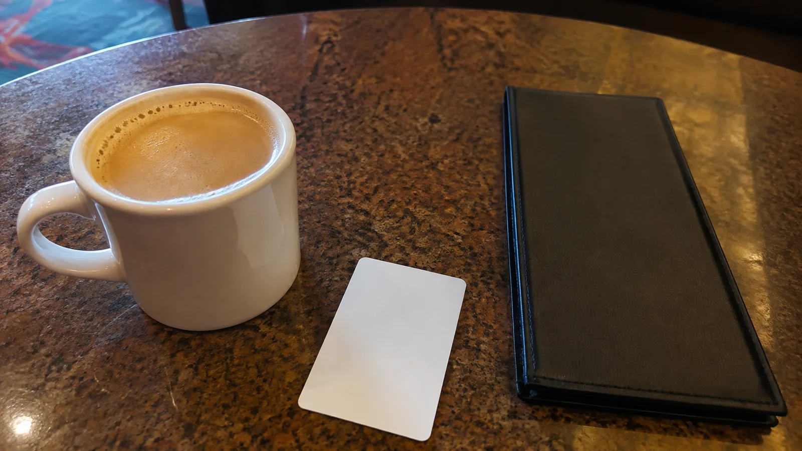 Coffee mug, plain white card and dark folder lie on a table.
