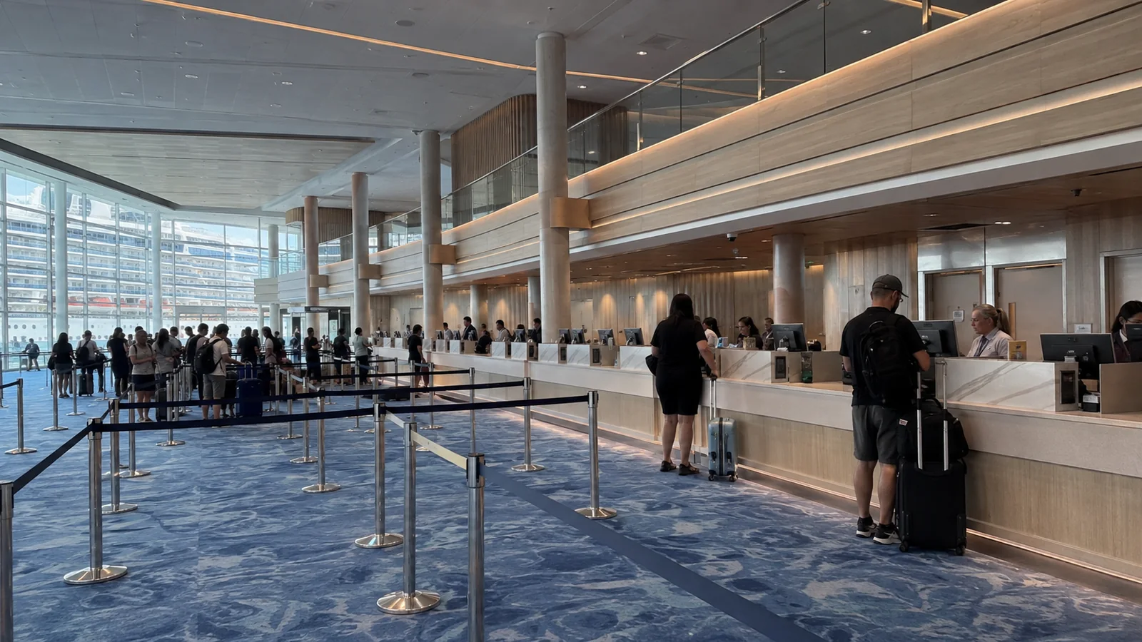 Travelers stand at counters inside a spacious terminal with queue barriers.