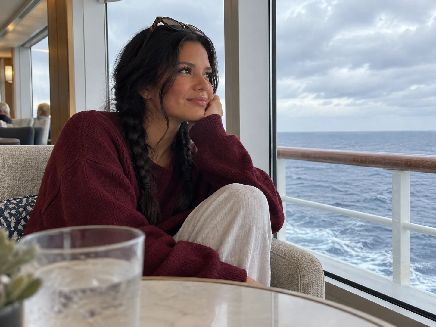 Ellie sits at an angle in an observation lounge with the sea beyond.