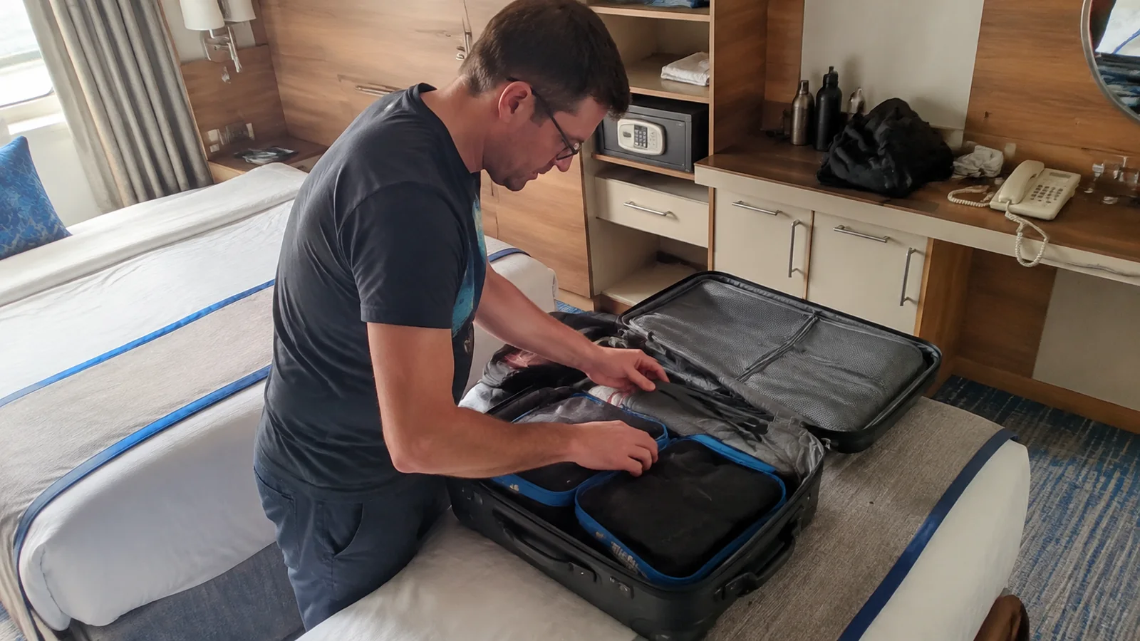 Man packs clothing into an open suitcase on a cabin bed.