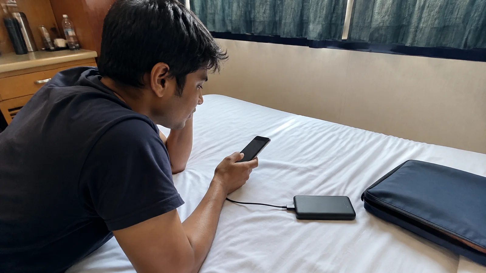 Man checks a phone connected to a portable charger on a bed.