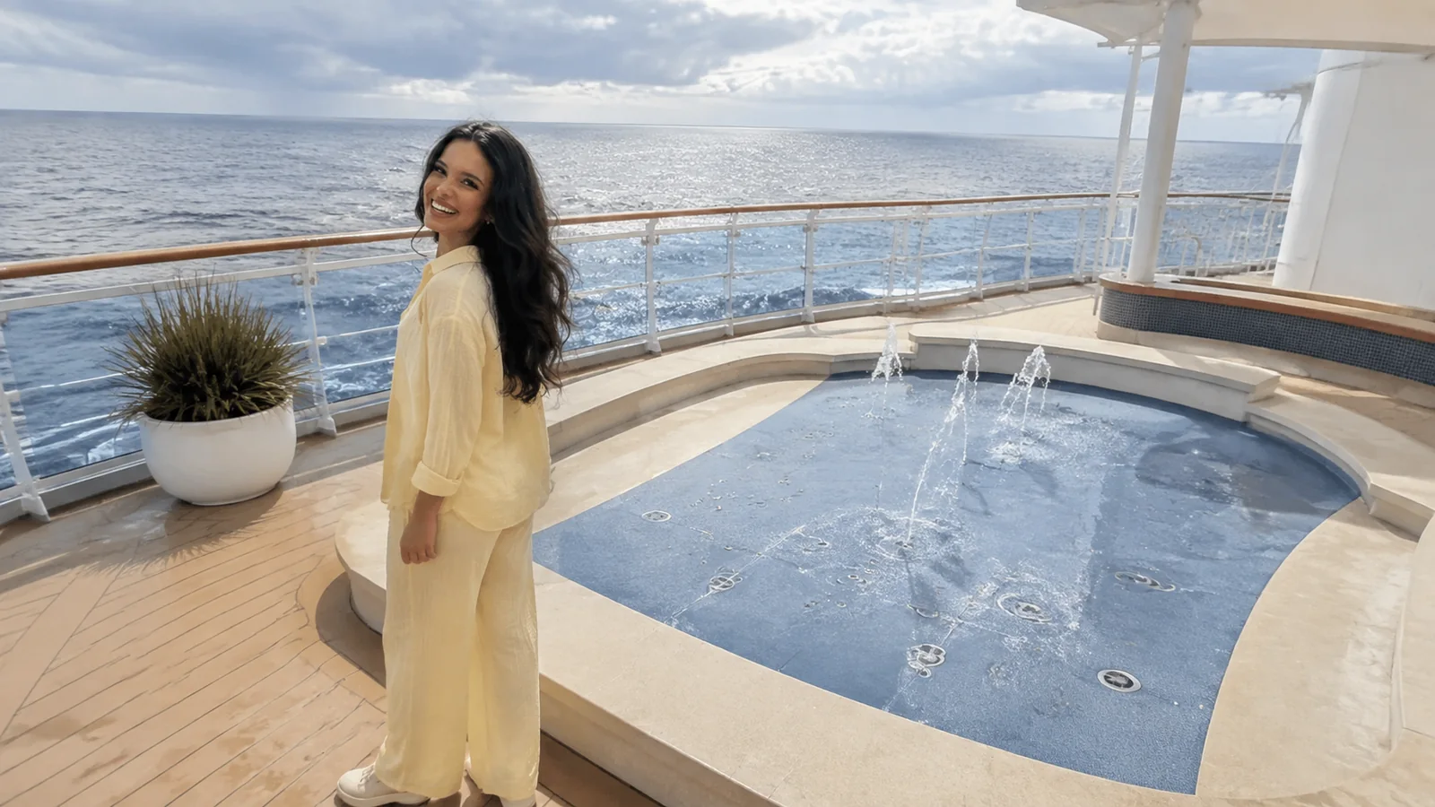 Woman standing beside a shallow splash pool on an ocean-facing deck.