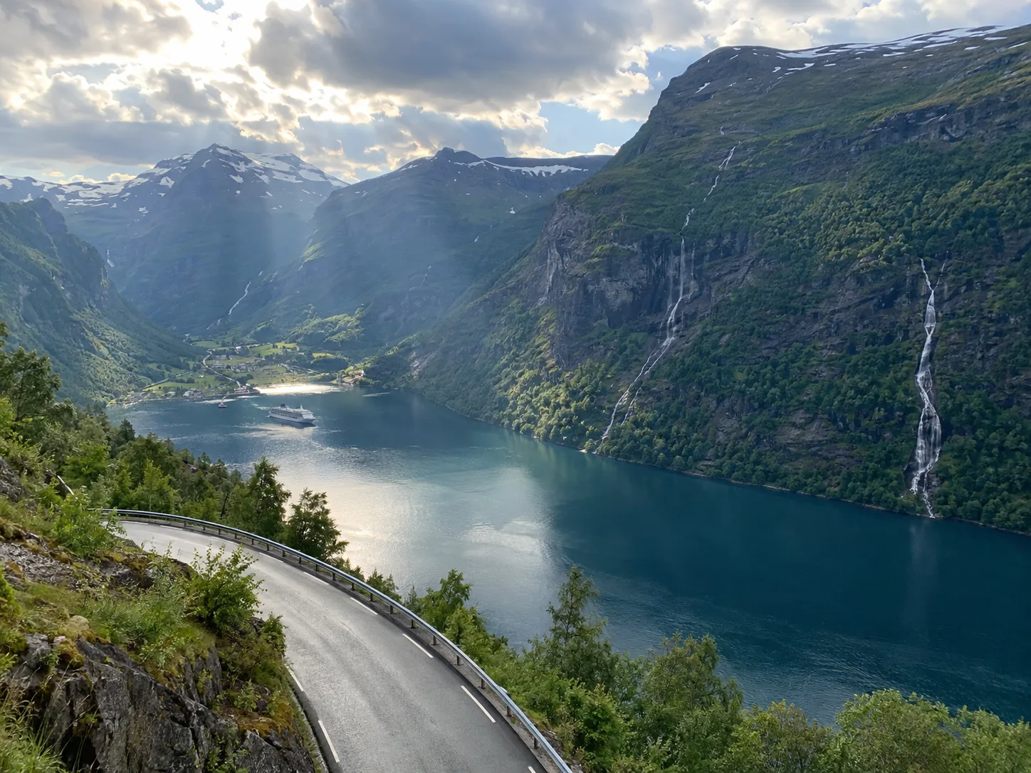 A cruise ship rests far below between steep mountains in Geirangerfjord.