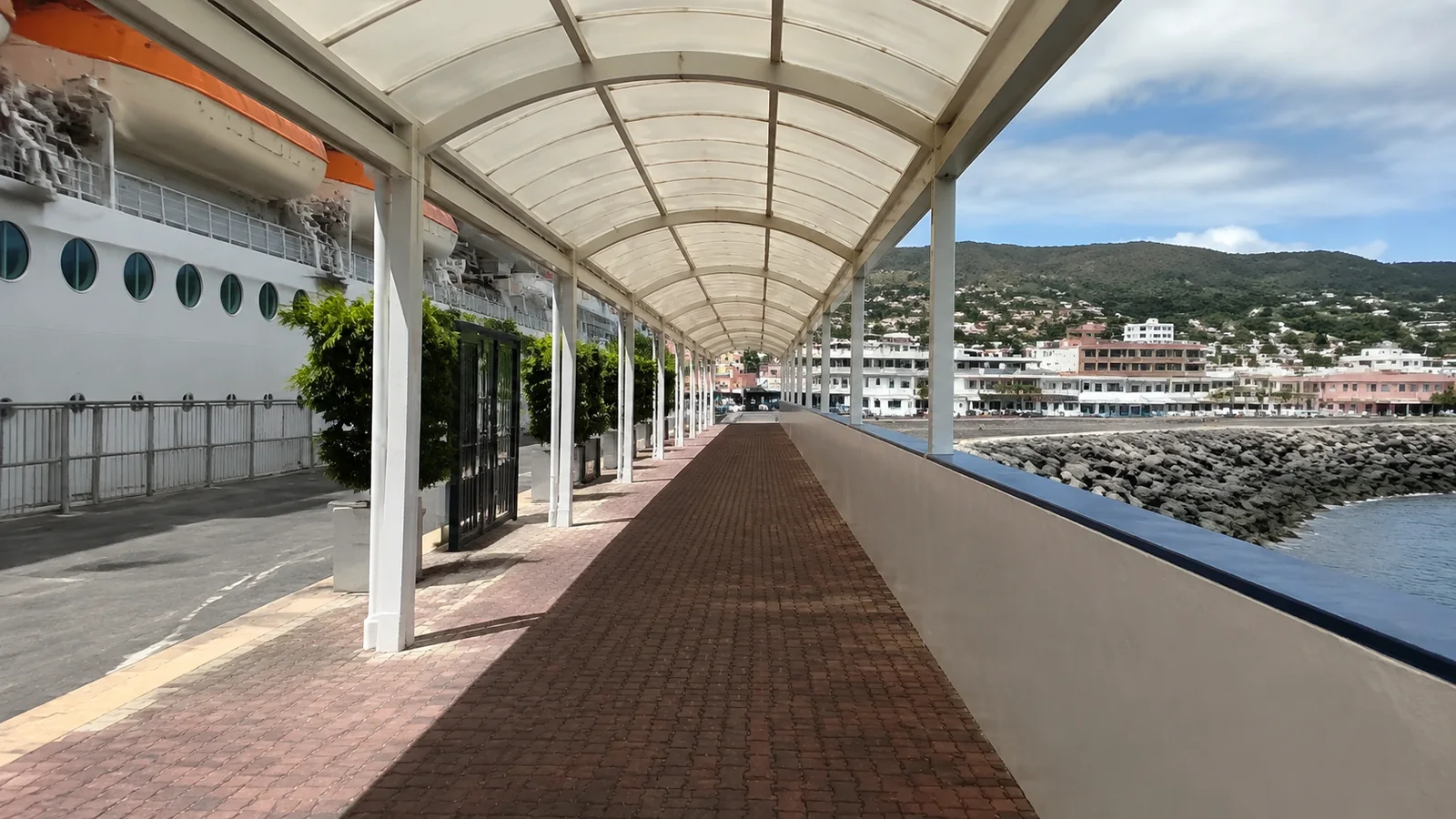 Covered walkway runs beside a docked ship and rocky waterfront.