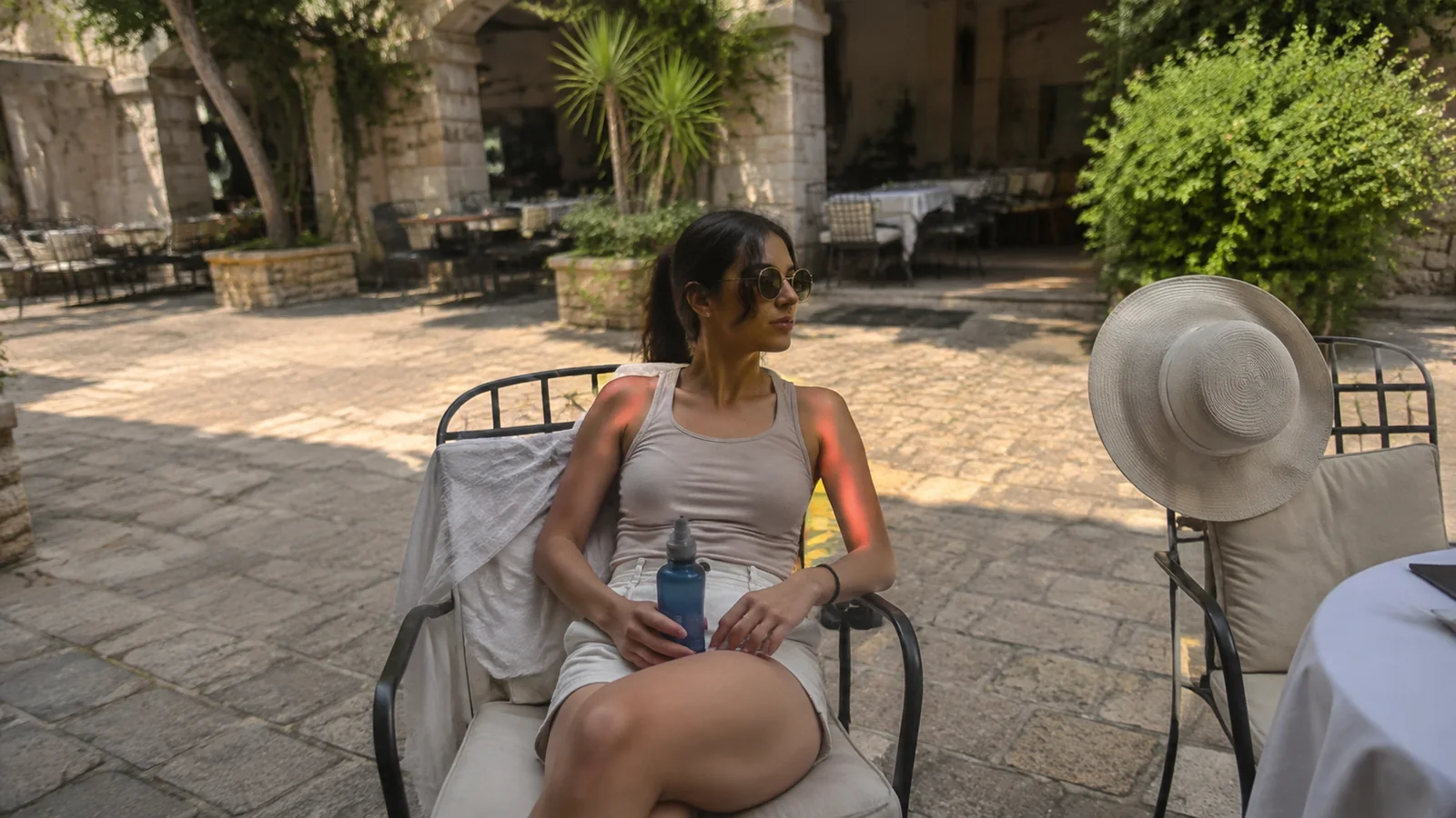 Woman resting at an outdoor courtyard table beside a sunhat.