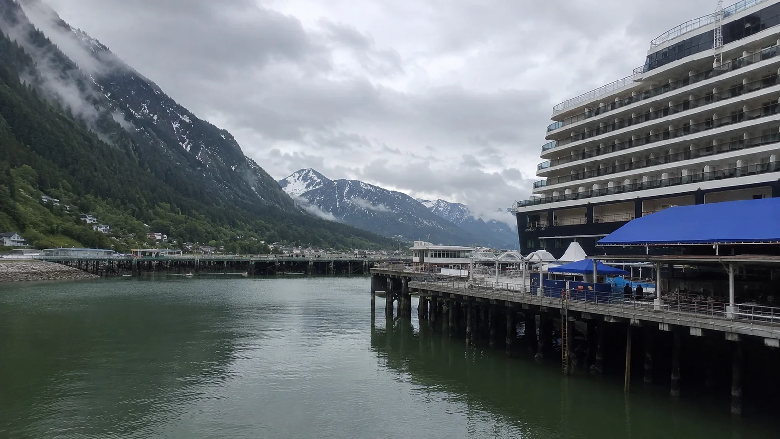Cruise ship docked at a mountain port under cloudy skies
