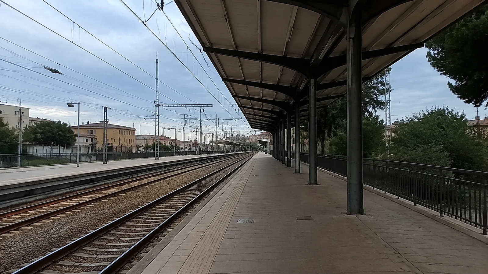 Empty railway platform beside multiple tracks beneath overhead wires.