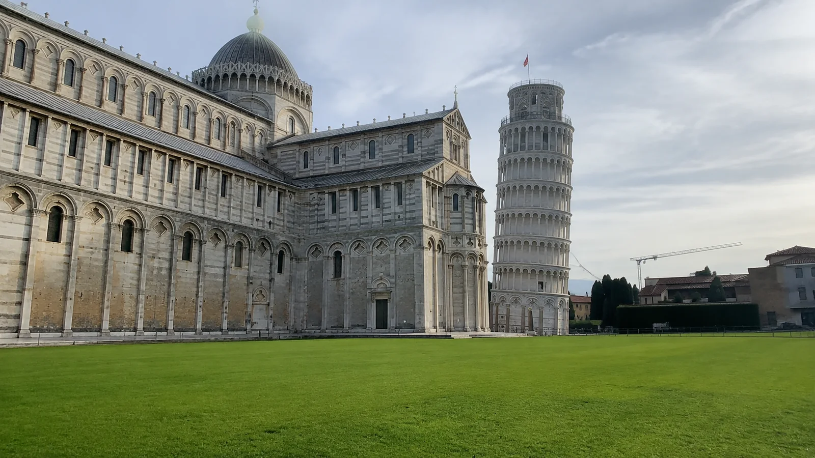 Leaning stone tower beside an ornate cathedral and green lawn.