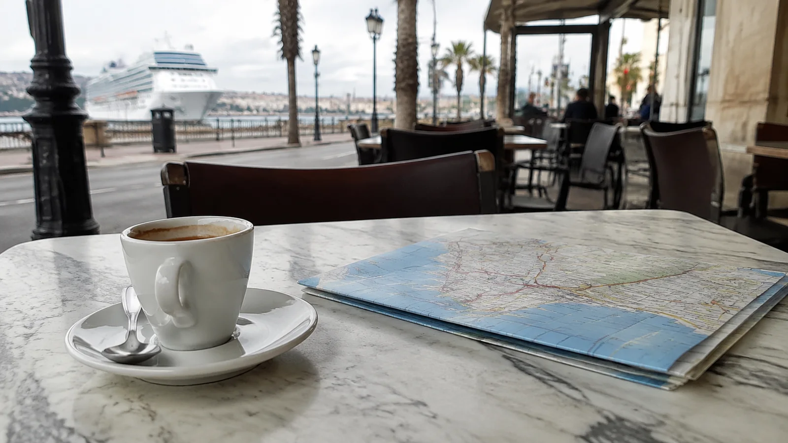 Coffee cup and map on a waterfront cafe table with a cruise ship beyond