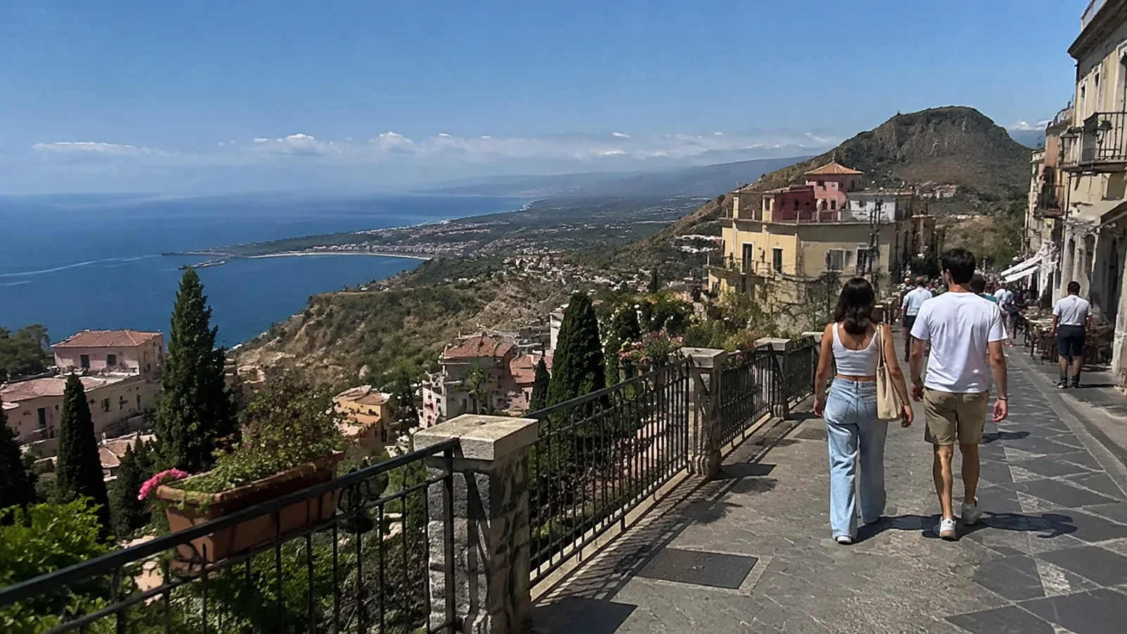 Travelers walking along a hillside promenade overlooking the sea